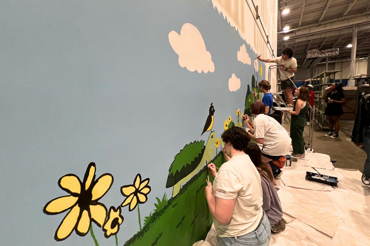 Students paint flowers, turtle, and blue sky on wall in Terrapin Trader
