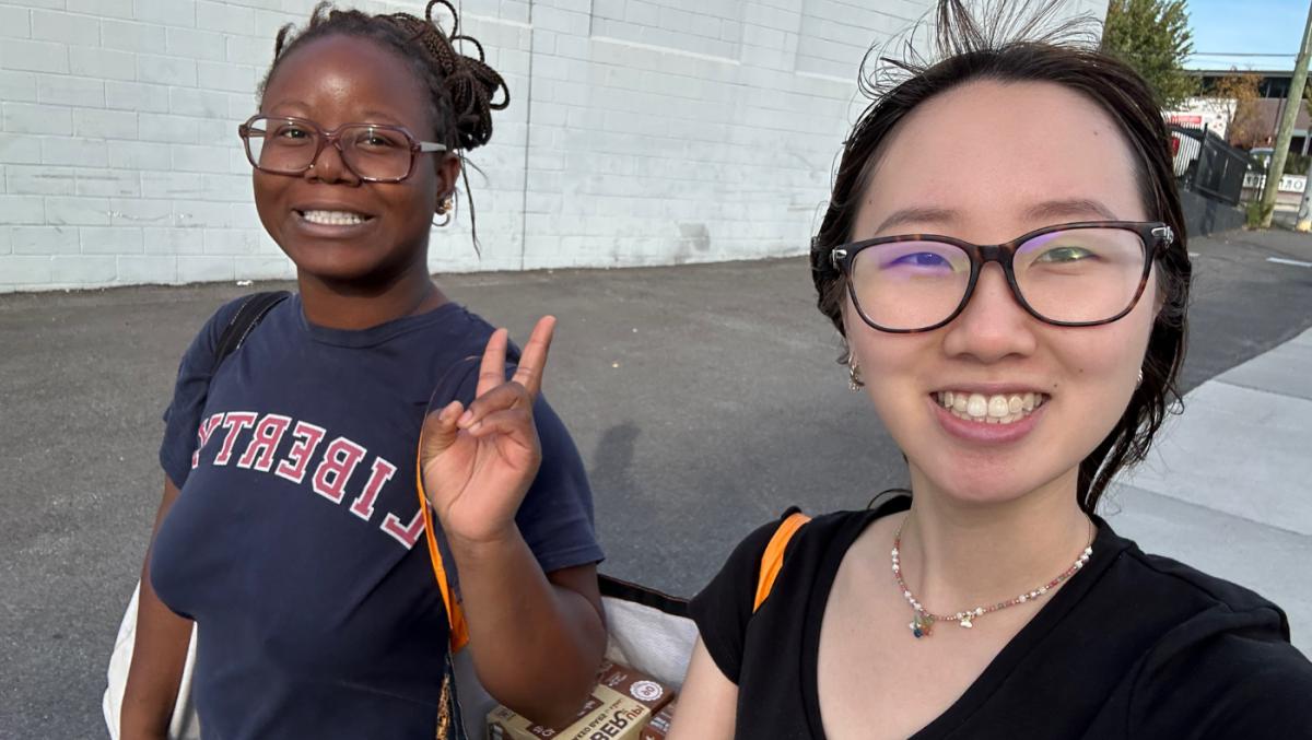 2 students carrying a reusable bag; one is holding up a peace sign