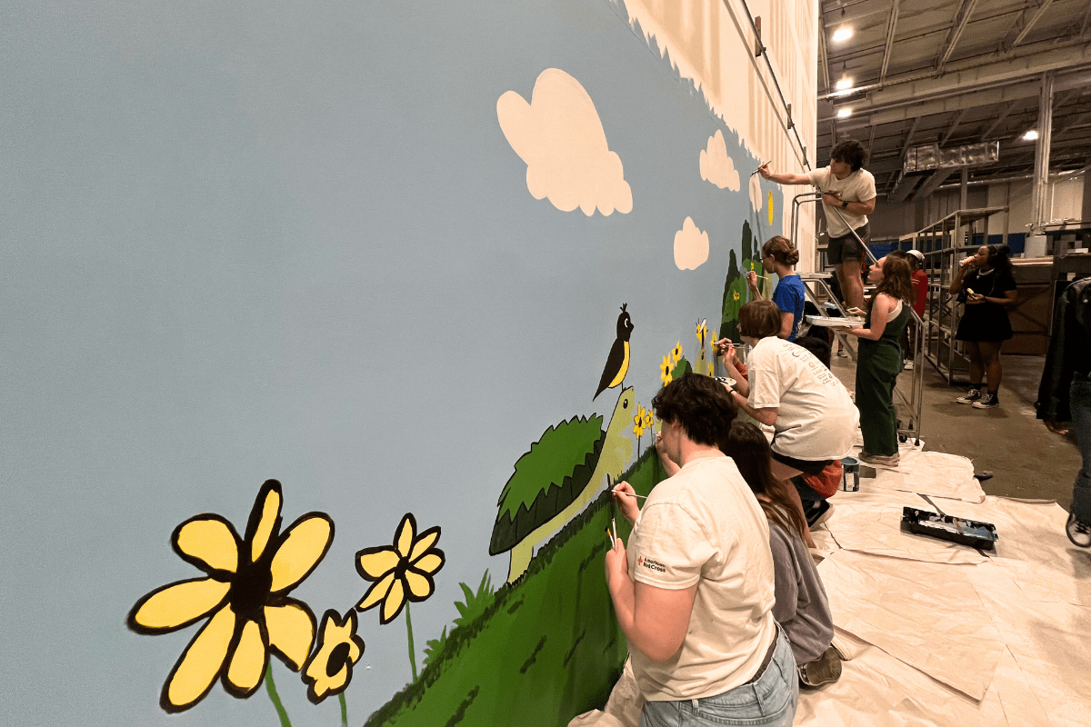 Students paint flowers, turtle, and blue sky on wall in Terrapin Trader