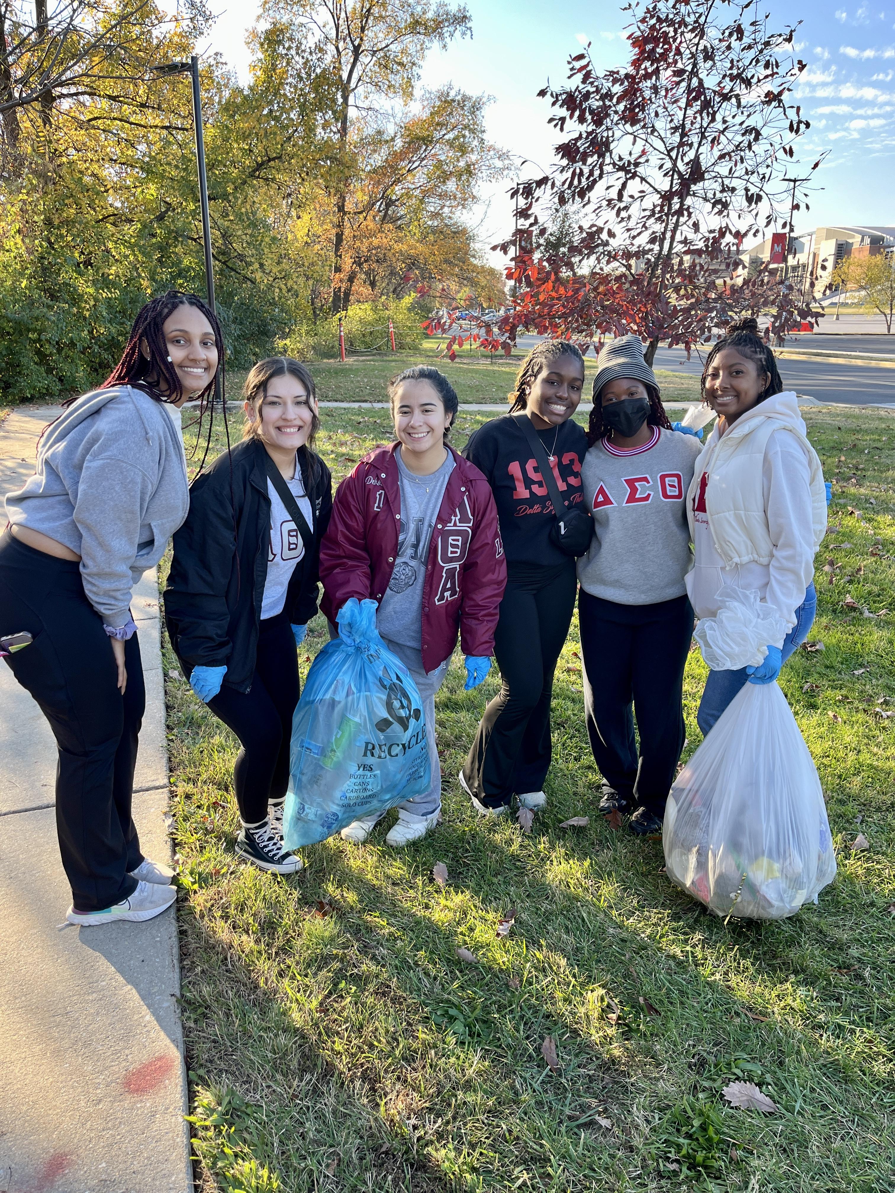 Students wearing Greek letters hold bags of collected litter.