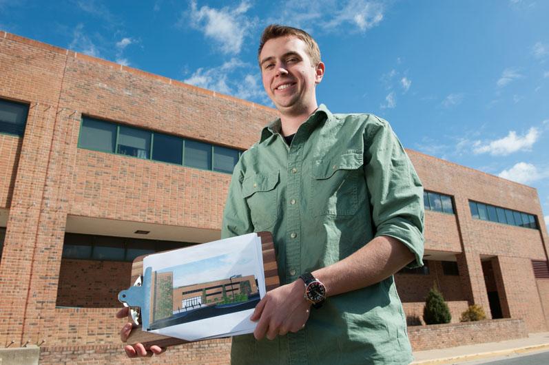 Student holding up a picture of a building in front of that building
