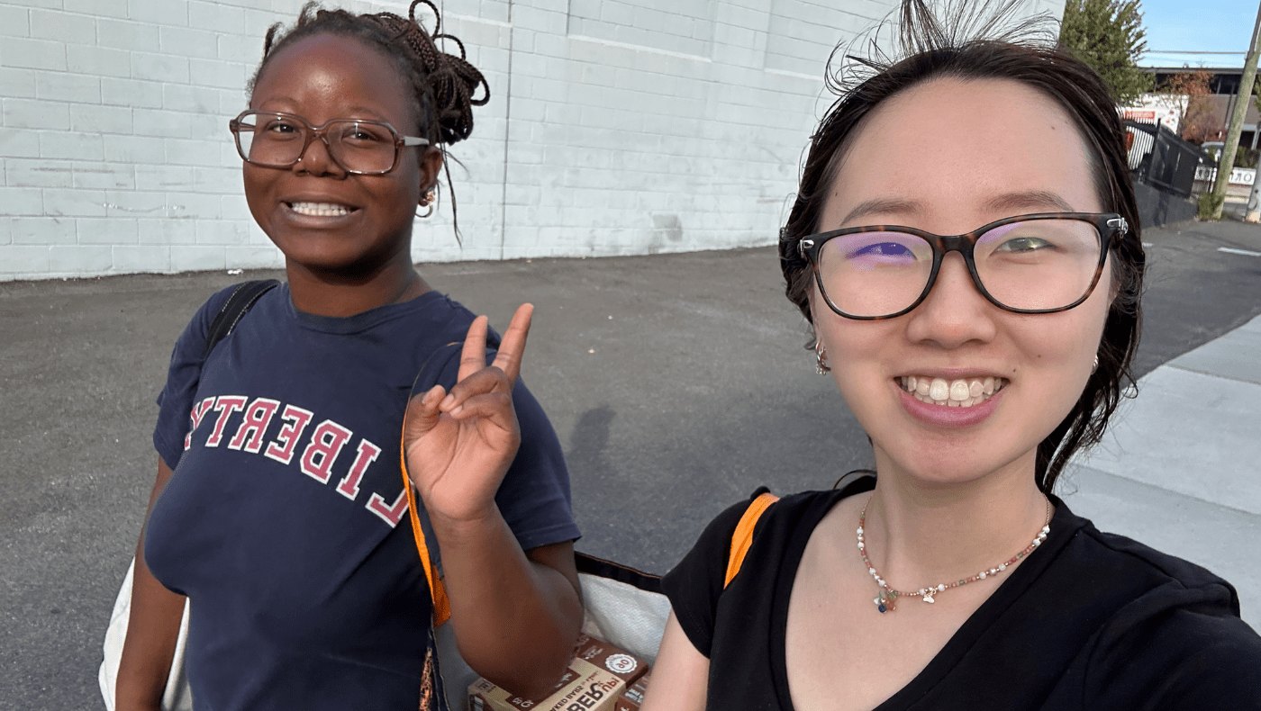 2 students carrying a reusable bag; one is holding up a peace sign