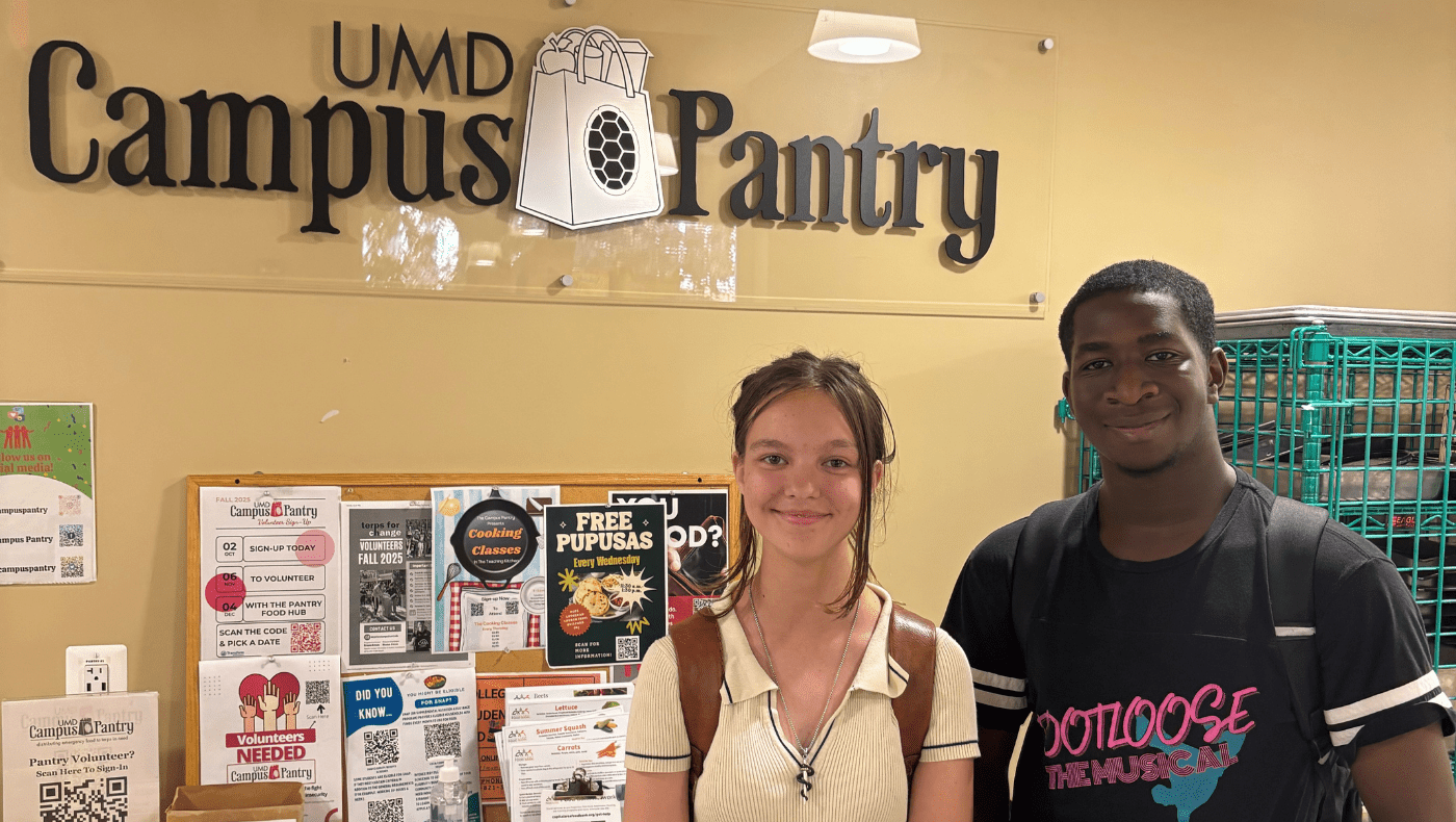 Two students standing in front of a UMD Campus Pantry sign