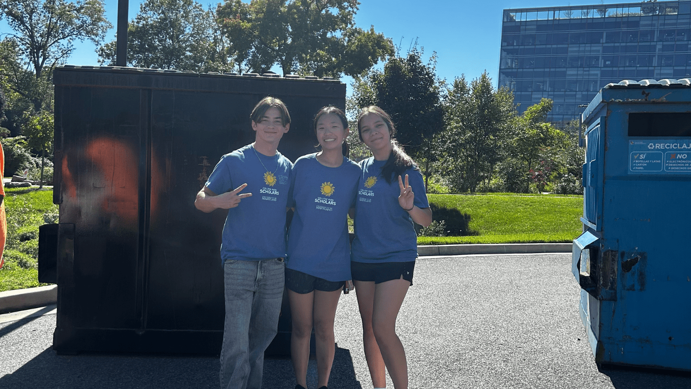 3 students posing in front of a dumpster after cleaning up trash