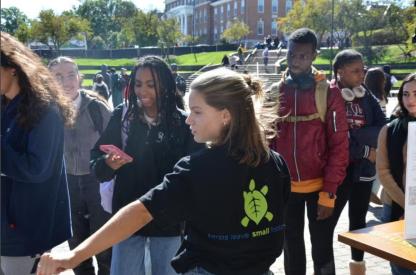 Student in SustainableUMD shirt points towards a sign 